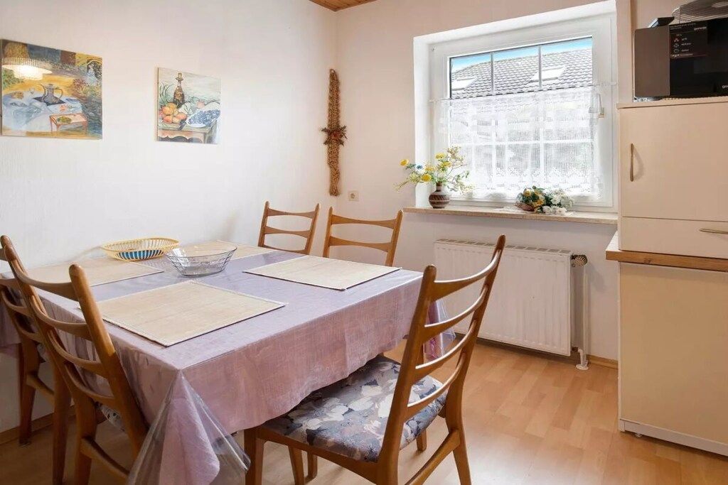 A dining area with a table set for four, wooden chairs, a window with a view, and a radiator below.