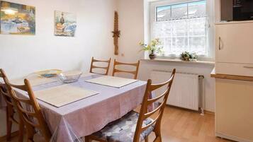 A dining area with a table set for four, wooden chairs, a window with a view, and a radiator below.