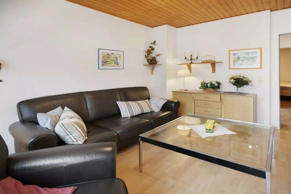 A living room with a leather sofa, a glass coffee table, and a wooden cabinet with a lamp.