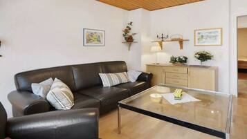 A living room with a leather sofa, a glass coffee table, and a wooden cabinet with a lamp.