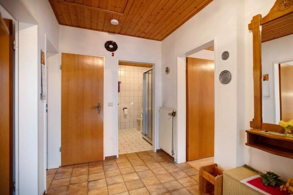 A hallway with wooden doors, a tiled floor, a mirror, and a radiator.