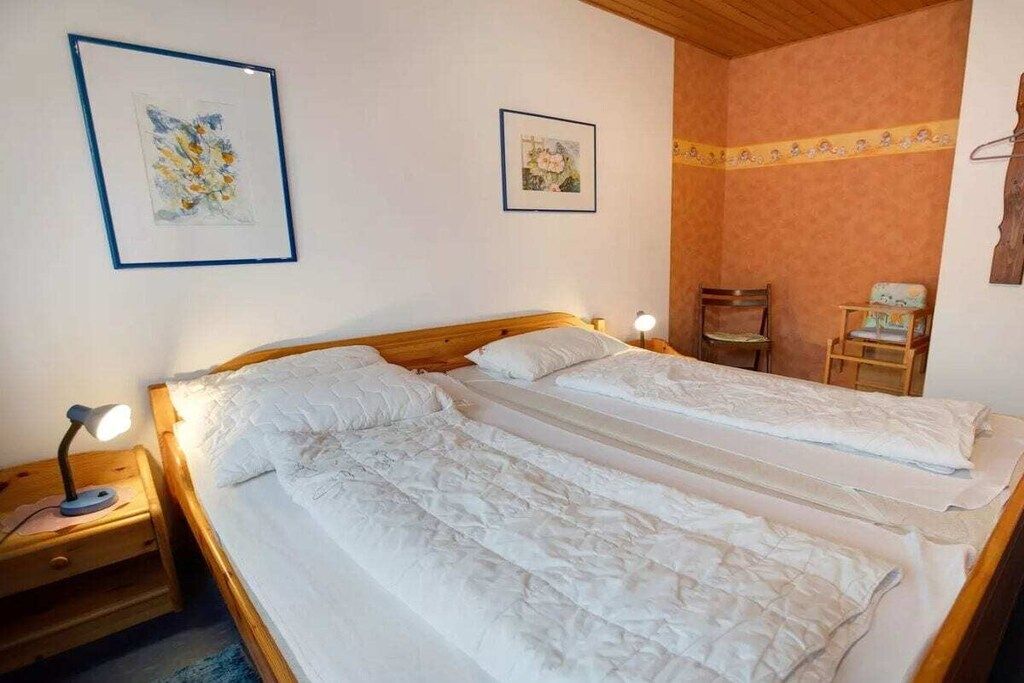 A double bed with white linens, a nightstand with a lamp, and two framed pictures on the wall.