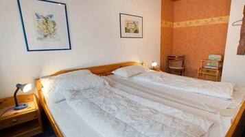 A double bed with white linens, a nightstand with a lamp, and two framed pictures on the wall.