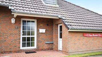 A brick building with a tiled roof, a numbered door, and a sign on the wall.