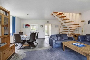 A modern living room with a staircase, a dining area, and a bookshelf. - Holiday home with 1 bedroom (Neßmersiel)