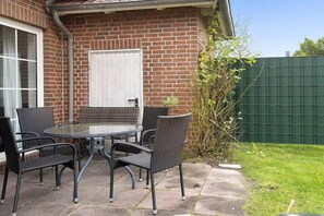 Une terrasse avec une table ronde et quatre chaises, un mur de briques, une porte blanche et une clôture verte.