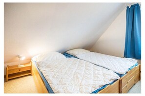 Quarto com uma cama de solteiro, mesa de cabeceira com abajur e cortina azul.