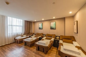 Um quarto com várias macas de massagem dispostas em linha, uma janela grande com cortinas e obras de arte nas paredes.