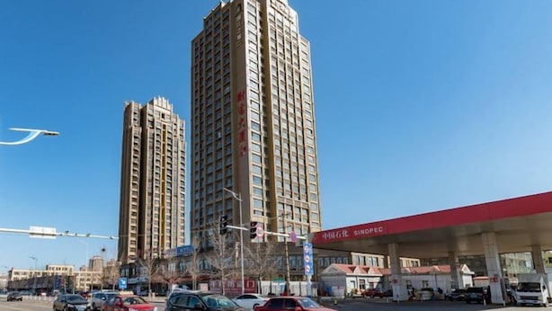 Um cruzamento urbano movimentado com edifícios altos, posto de gasolina e veículos.