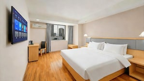 Quarto de hotel com cama, mesas de cabeceira, escrivaninha, cadeira, televisão fixada na parede e janela com cortinas.