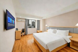 Habitación de hotel con cama, mesitas de noche, escritorio, silla, televisor montado en la pared y ventana con cortinas.