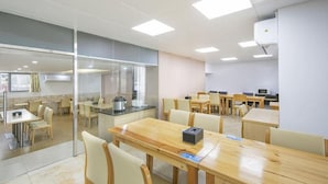 Uma zona de refeições moderna, com várias mesas e cadeiras, área de cozinha com eletrodomésticos e um painel de vidro.
