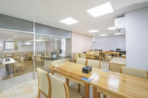 Un comedor moderno con varias mesas y sillas, una zona de cocina con electrodomésticos, y un separador de vidrio.