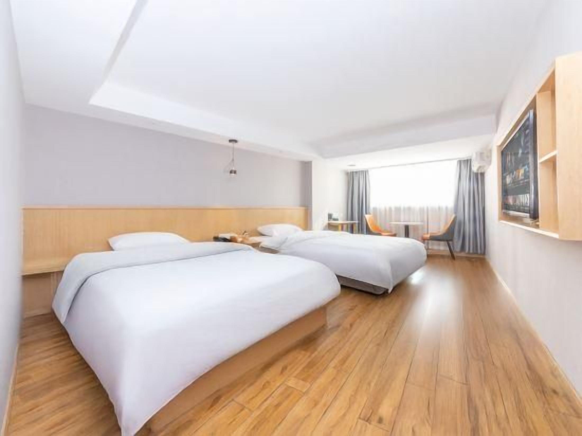 A hotel room with two beds, wooden flooring, a large window, and a view of the outdoors.