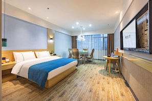 A hotel room with a large bed, a desk with a chair, a television, and a window with curtains. - City Convenient Hotel (Hengyang)