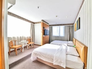 Habitació d'hotel amb dos llits, zona de seients amb cadires i taula, i un televisor fixat a la paret.