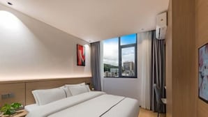 A hotel room with a large bed, a desk, a chair, a window with a city view, and a wall-mounted TV. - Super 8 Quanzhou Anxi Longhu (Quanzhou)