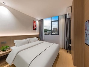 Habitació d'hotel amb un llit gran, escriptori, cadira, finestra amb vista a la ciutat i televisió penjada a la paret.