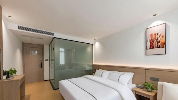 A hotel room with a bed, bedside table, and a glass partition wall. - Super 8 Quanzhou Anxi Longhu (Quanzhou)