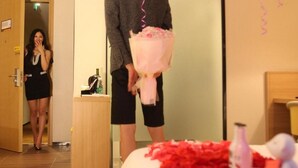 A hotel room with a bed, a mirror, and a person holding a bouquet. - IU Hotel (Luoyang)