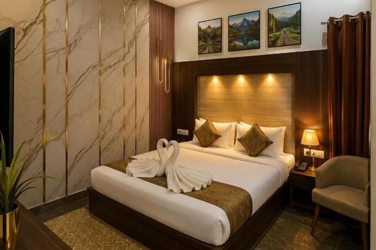 A hotel room with a bed, a ceiling fan, a nightstand, a lamp, a chair, and a wall-mounted TV.