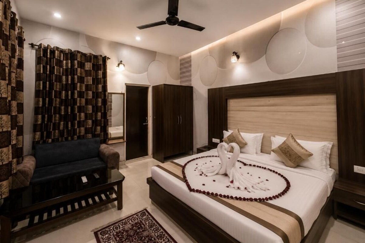 A hotel room with a bed, a sofa, a ceiling fan, and a patterned curtain.