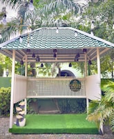 Un pabellón con techo verde, un letrero que dice 'Hotel Green Garden', y un área de acceso pavimentada con un pequeño jardín.