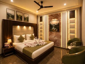 A hotel room with a large bed, a ceiling fan, a nightstand with a lamp, and a chair. - Hotel Green Garden (Ludhiana)