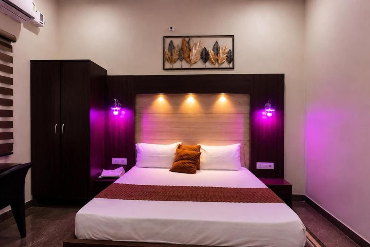 A hotel room with a large bed, a wardrobe, a nightstand, and a wall-mounted artwork.