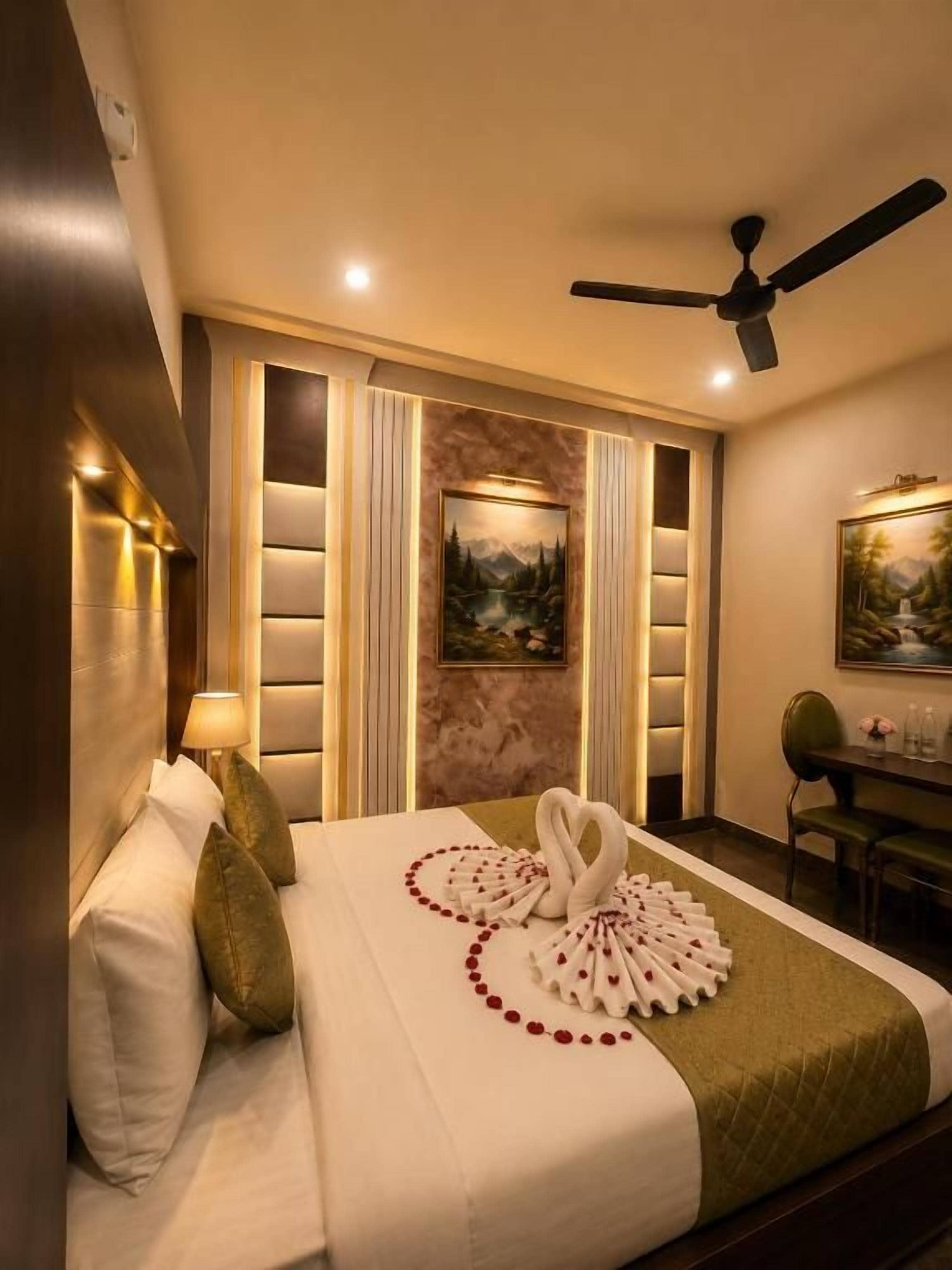 Habitación de hotel con cama, almohadas, un cuadro en la pared, ventilador de techo y un escritorio con sillas.