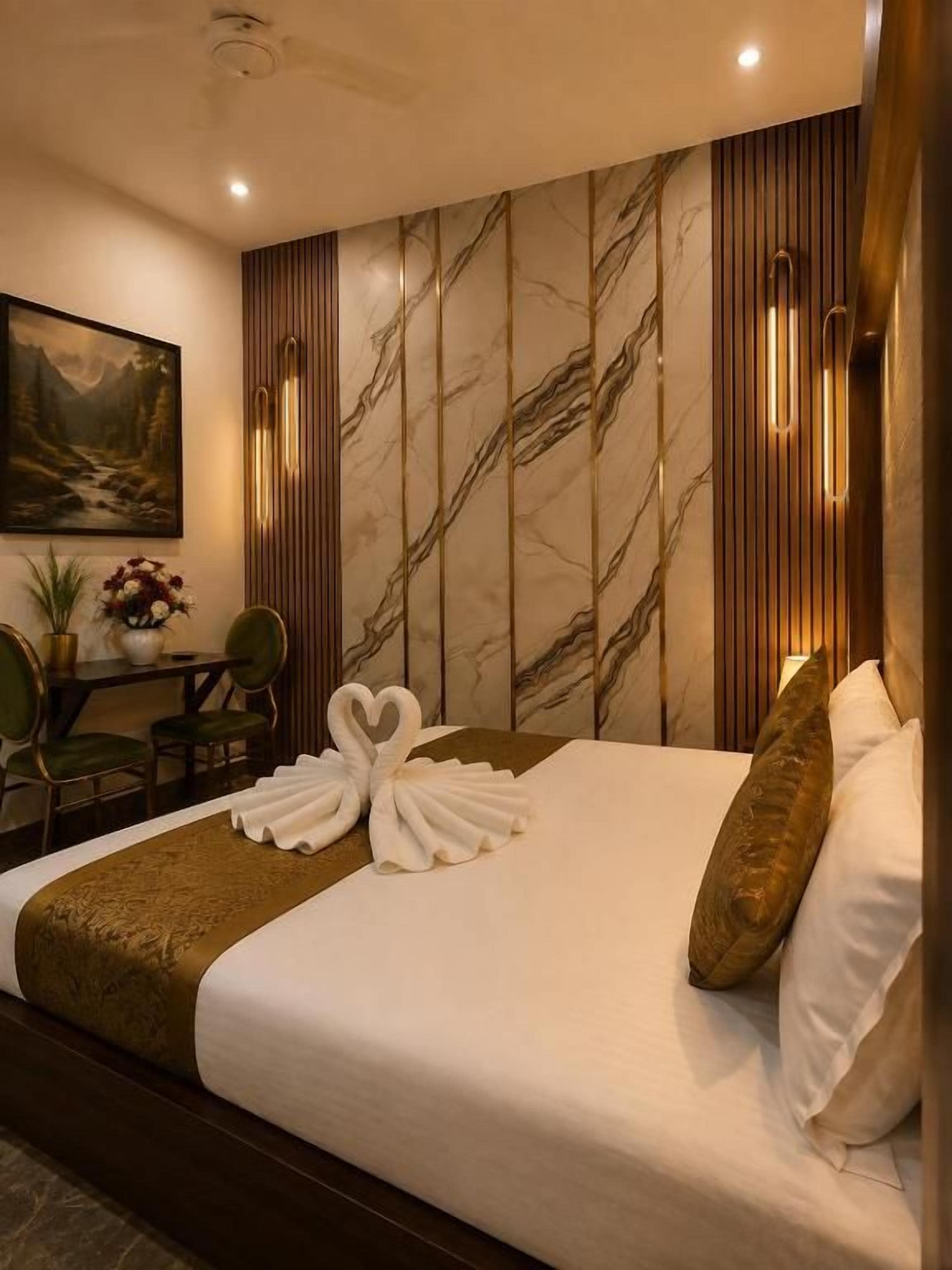 Una habitación de hotel con una cama, una sala de estar con sillones, una mesa con un jarrón de flores y un cuadro en la pared.