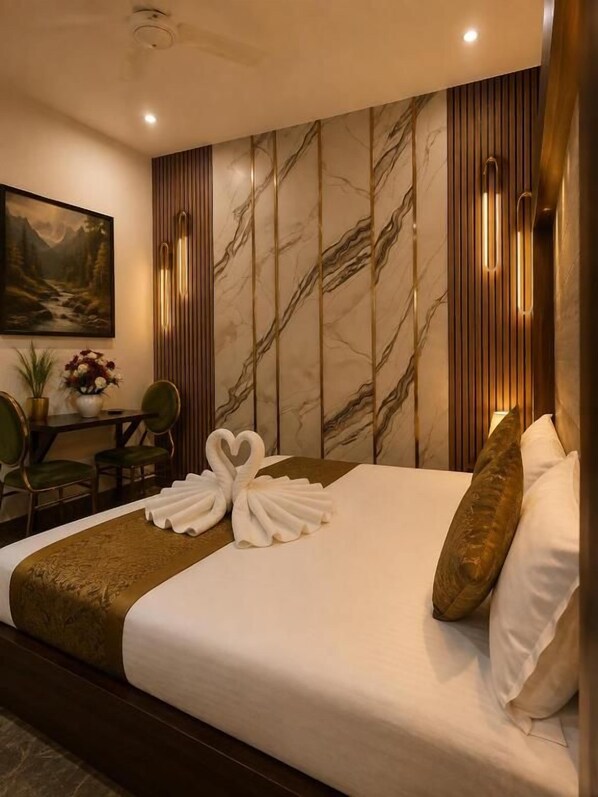 Una habitación de hotel con una cama, una sala de estar con sillones, una mesa con un jarrón de flores y un cuadro en la pared.