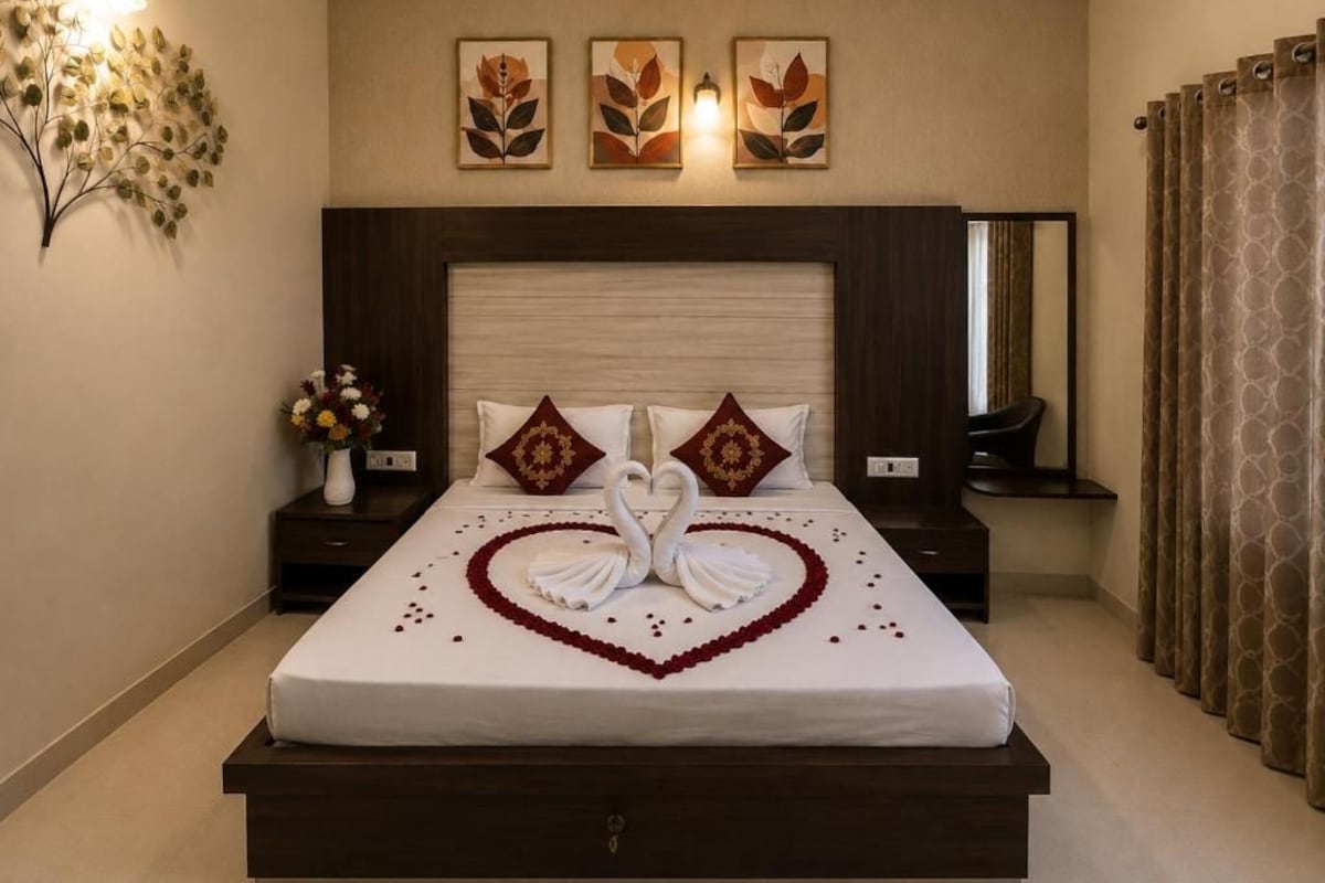 A hotel room with a large bed, a nightstand with a vase of flowers, and wall-mounted artwork.