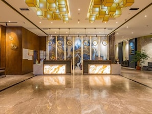 Un área de recepción con suelo de mármol, un mostrador de recepción y una pared con arte abstracto.