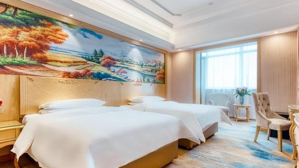 A hotel room with two beds, a large mural on the wall, a desk, and a chair. - Vienna International Hotel (Tianjin)