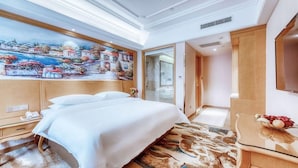 A hotel room with a large bed, a painting on the wall, a desk with a fruit bowl, and a mirror. - Vienna International Hotel (Tianjin)