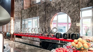 A buffet setup with various food items and a marble wall with a circular window. - Vienna International Hotel (Tianjin)
