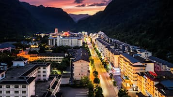 A town with a long street lined with buildings, a prominent hotel with a tower, and mountains in the background.