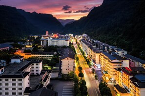 A town with a long street lined with buildings, a prominent hotel with a tower, and mountains in the background.
