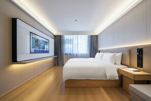 A hotel room with a large bed, bedside tables, a TV mounted on the wall, and a view of the outdoors through the window.
