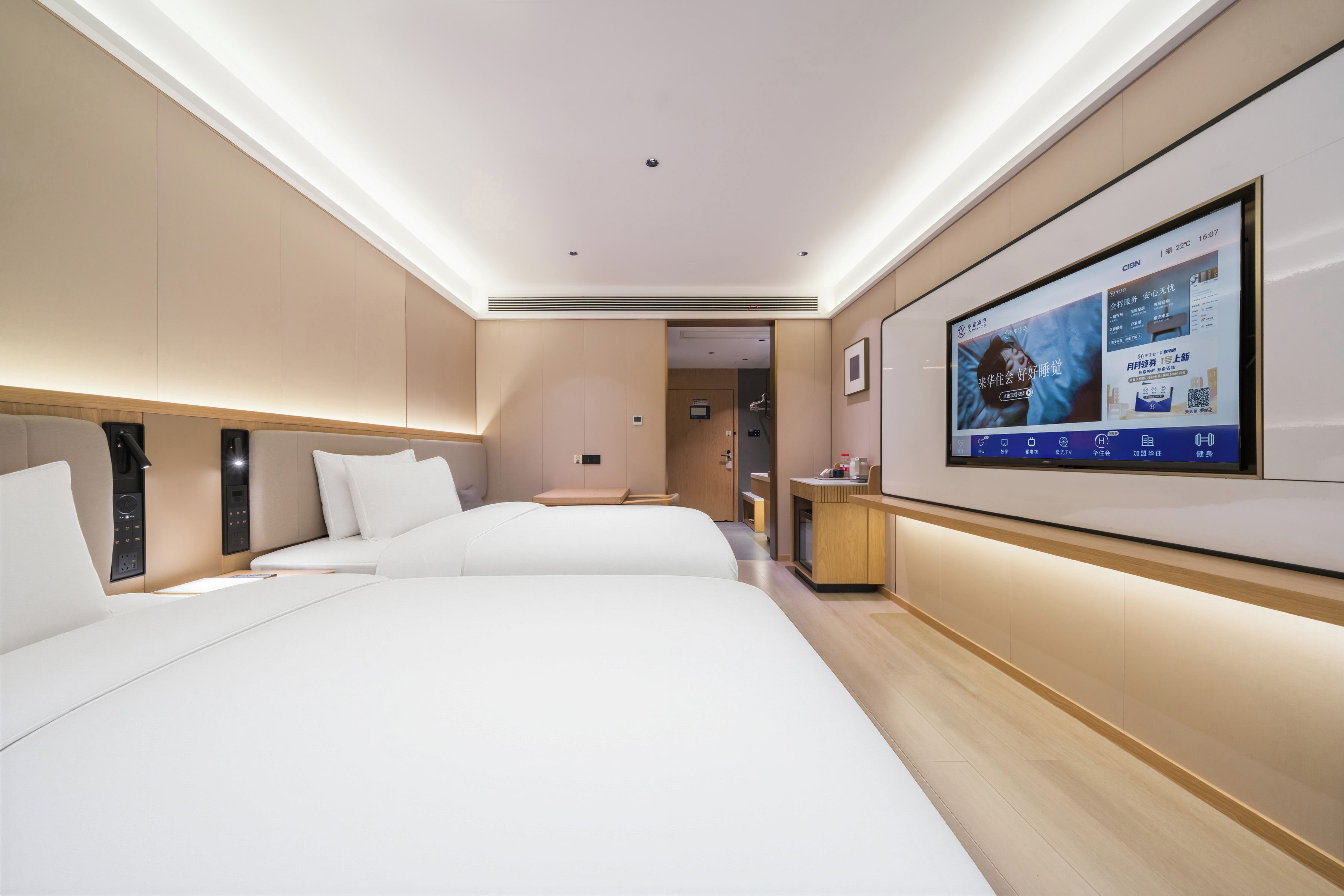 A modern hotel room with two beds, a flat-screen TV mounted on the wall, and a wooden desk with a chair.