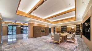 En rummelig hotellobby med et marmorgulv, et centralt spiseområde med borde og stole, samt en receptionsdisk.