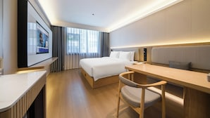 Et moderne hotelværelse med seng, skrivebord, stol og et stort vindue.