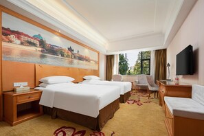 A hotel room with two beds, a desk, a chair, a TV, and a painting of a cityscape. - Vienna 3 Best Hotel (Wuhan)