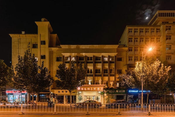 A multi-story hotel with a prominent entrance, a parking area, and various commercial establishments in the foreground. - Vienna 3 Best Hotel (Wuhan)