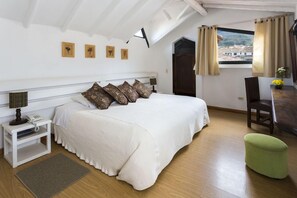 Een slaapkamer met een bed, nachtkastje, lamp en uitzicht op een stadsbeeld door een raam.