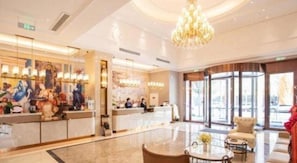 Et hotellobby med reception, siddeområde og store vinduer.