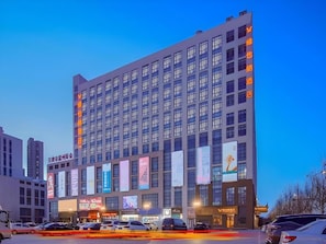 Et hotel med flere etager, en moderne facade, store vinduer og flere bannere, der reklamerer for diverse tilbud.