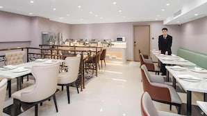 A hotel dining area with multiple tables and chairs, a buffet setup, and a staff member present. - Vienna Hotel (Tianjin)
