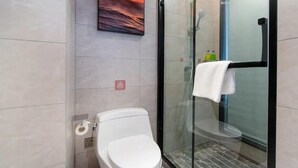 A modern bathroom with a glass shower enclosure, a toilet, and a wall-mounted sink. - Vienna Hotel (Tianjin)